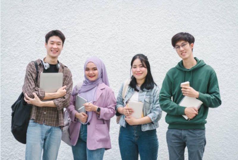 Group of Singapore university students and tutors standing together with books and notebooks.