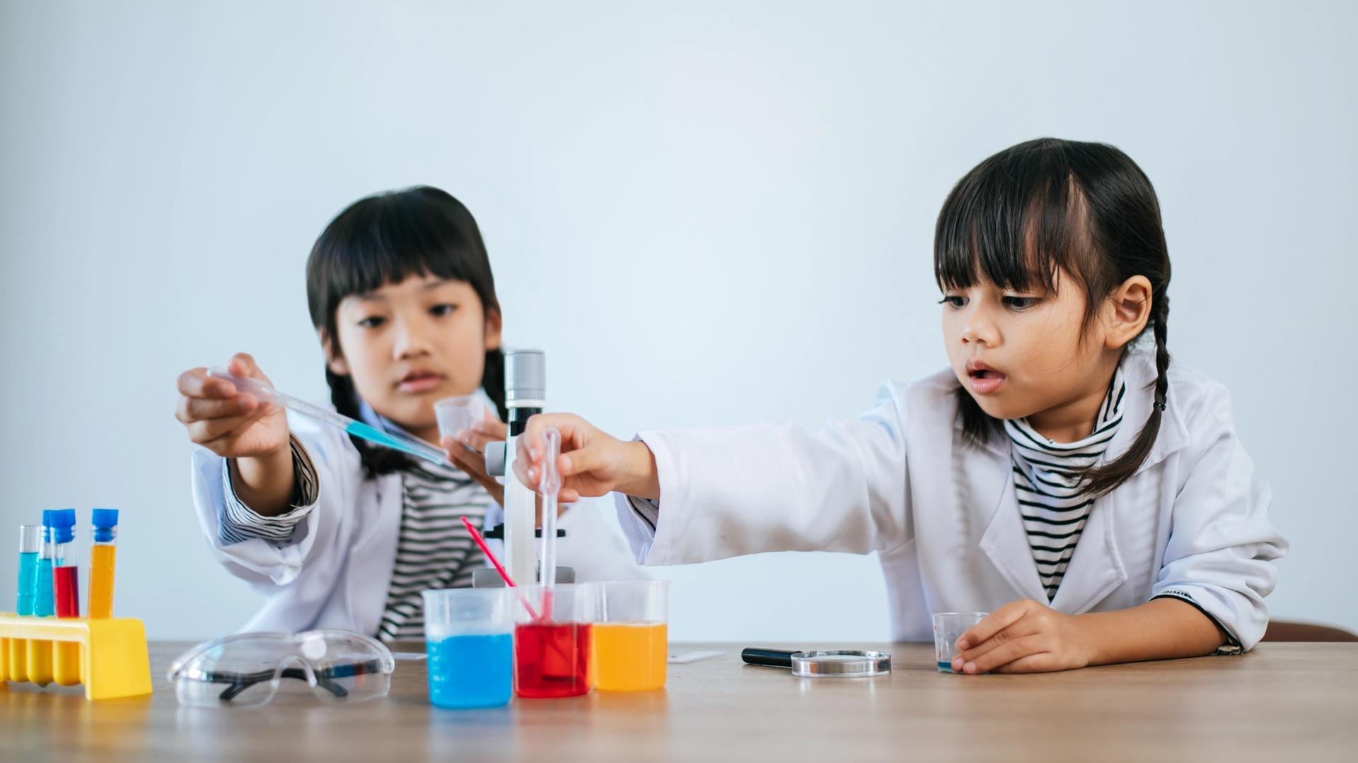 Two young children in lab coats performing a colorful science experiment.