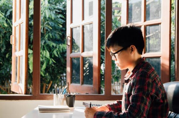Secondary school student studying at a desk during golden hour sunlight near a window