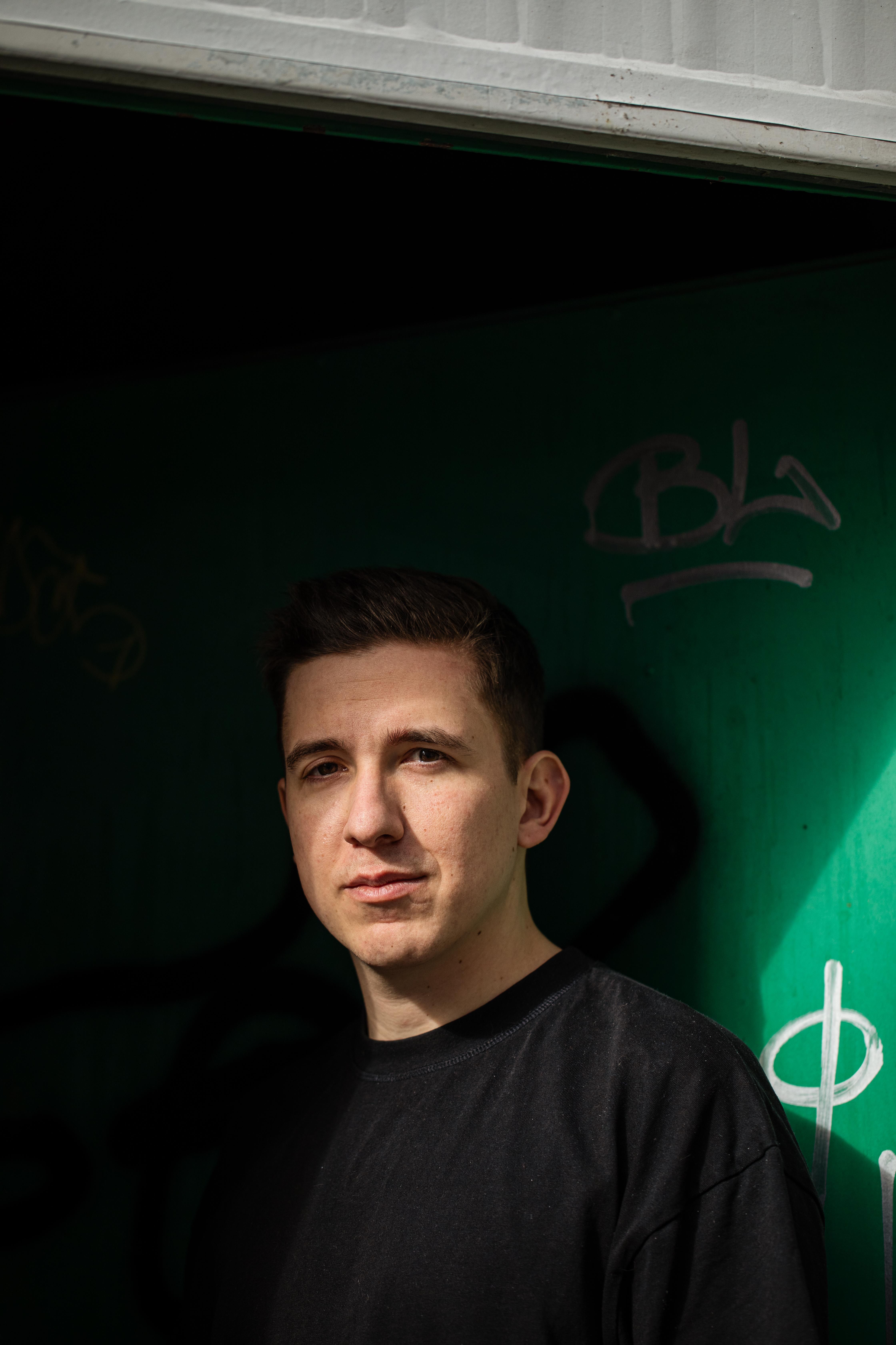 Portrait von Maurizio Zulli vor einer gruen beleuchteten Wand mit Graffiti.