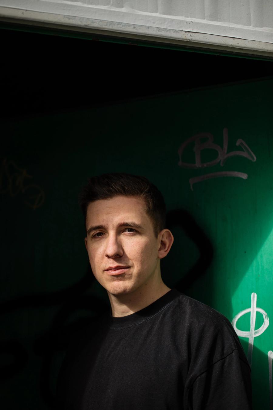 Portrait von Maurizio Zulli vor einer gruen beleuchteten Wand mit Graffiti.