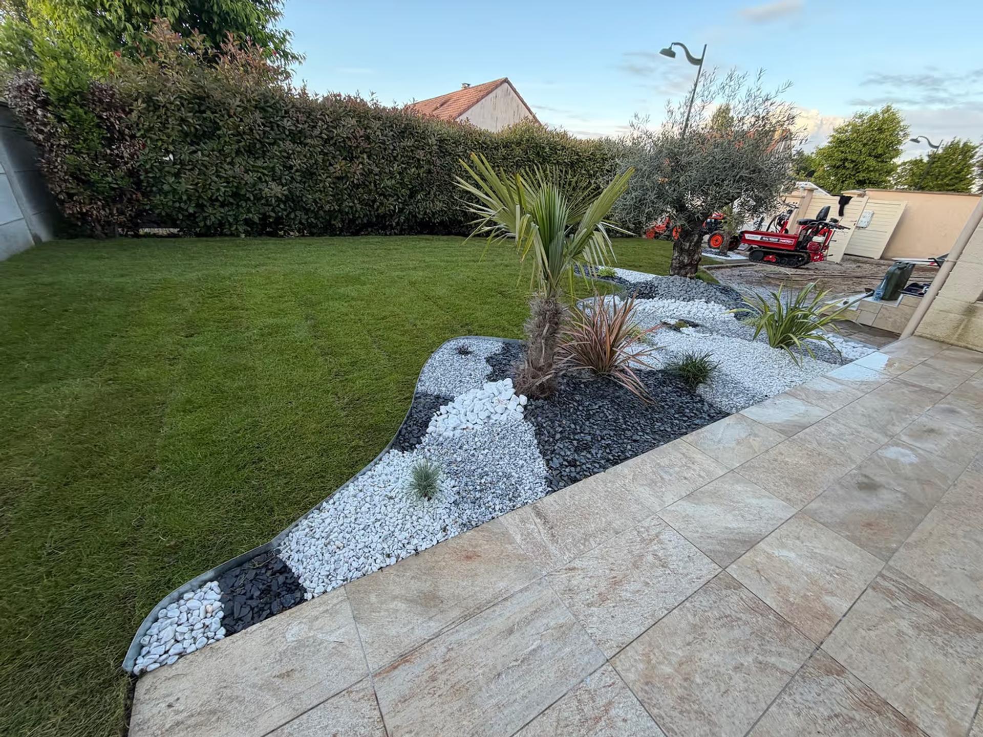 Terrasse en pierre et massif de galets blancs et noirs planté de palmiers, pelouse tondue en raies