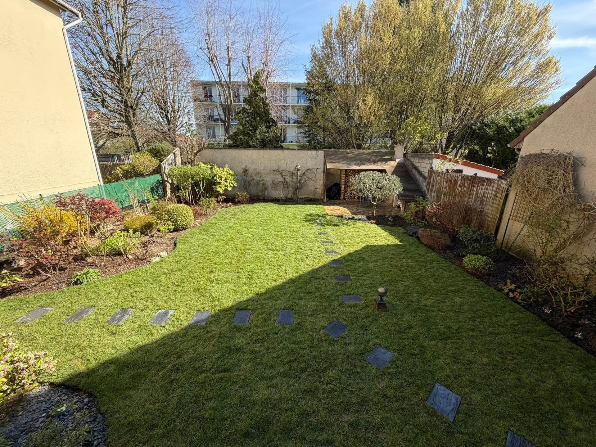Jardin de ville engazonné avec des pas japonais en ardoise et des massifs en bordure