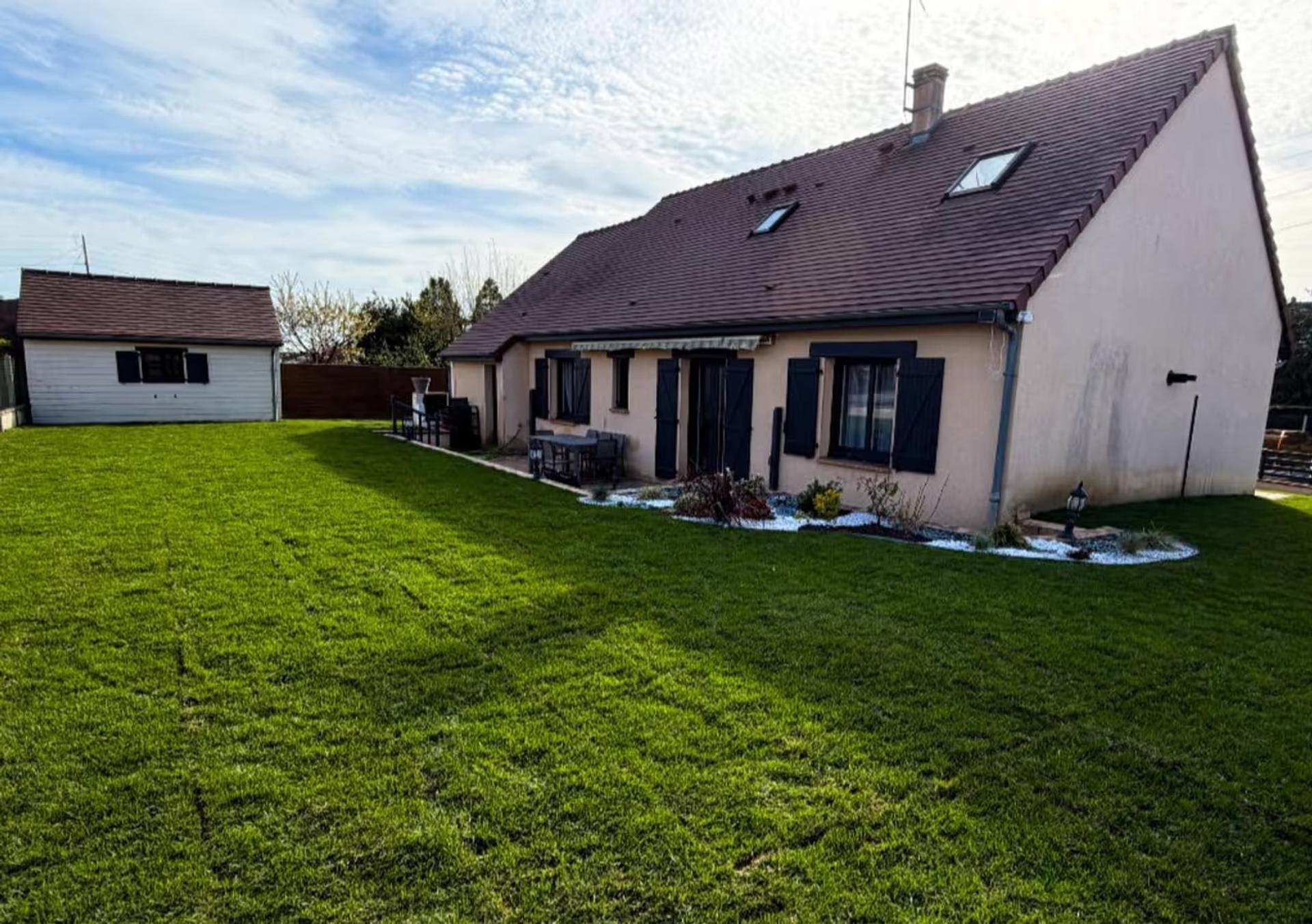 Grande pelouse tondue en bandes devant un pavillon, avec un massif de galets au pied de la façade