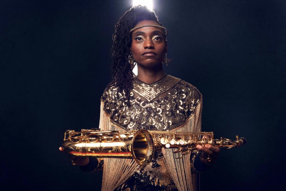 Lakecia Benjamin holding her saxophone wearing a gold dress