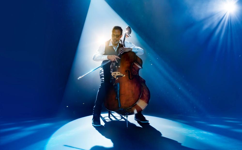 Stanley Clarke playing his upright bass under a spotlight, with blue light around him.