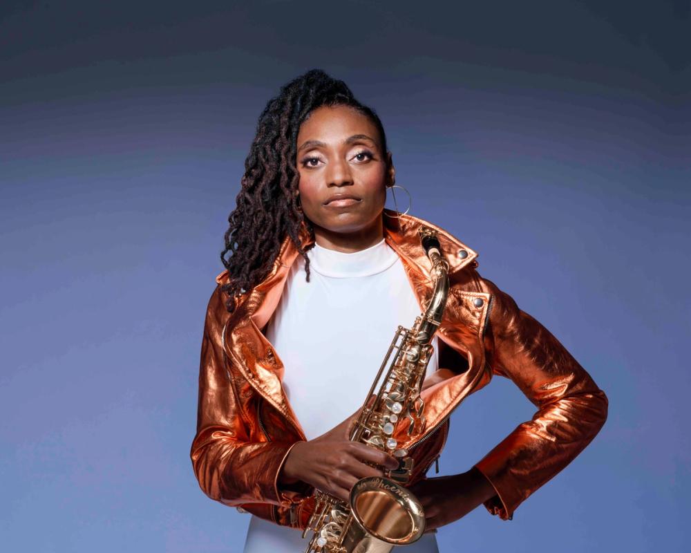 Lakecia Benjamin holding her saxophone wearing a gold jacket and white shirt