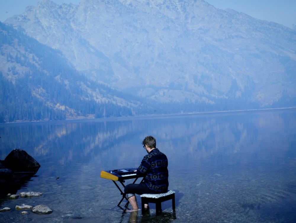 Elijah Fox playing his keyboard in a lake in the mountains