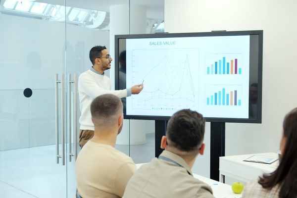 Man presenting charts on a large screen to audience.