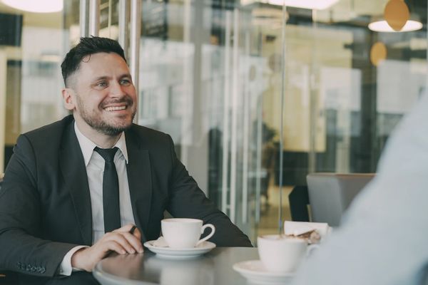Two men in suits having coffee at a table.
