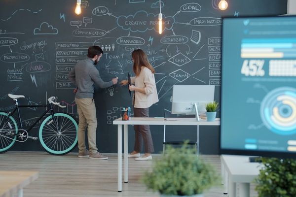 Two people collaborating on a chalkboard with a bicycle.