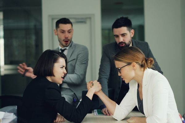 Two women arm wrestling with men watching