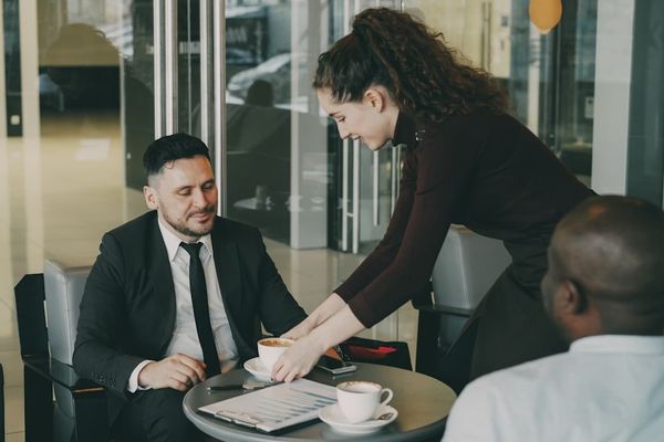 Waitress serving coffee to two businessmen in cafe.