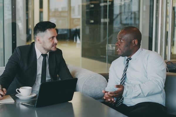 Two businessmen in suits talking in a modern office.