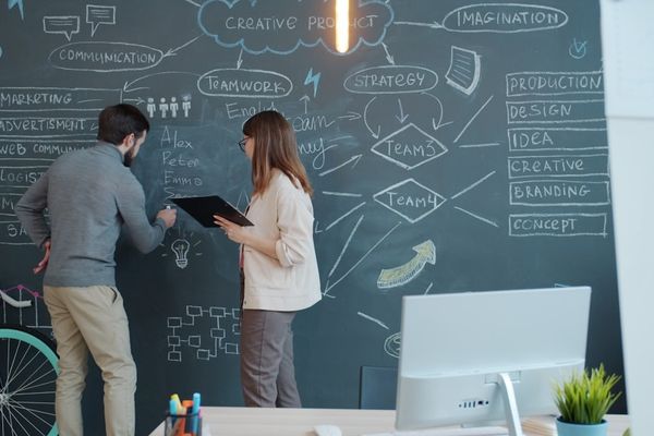 Two people brainstorming on a chalkboard wall.