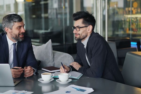 a couple of men sitting at a table in front of a laptop