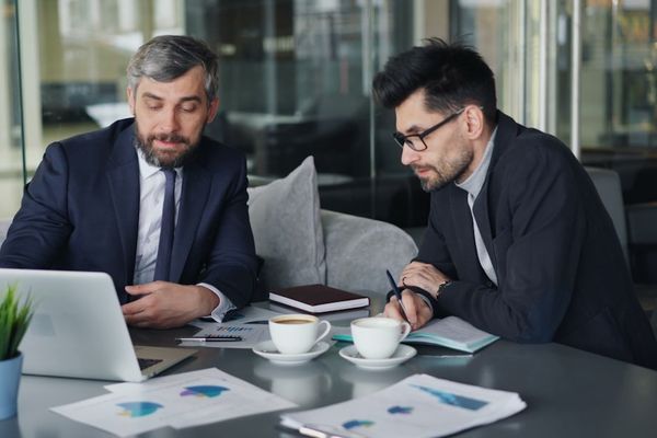 two men sitting at a table working on a laptop