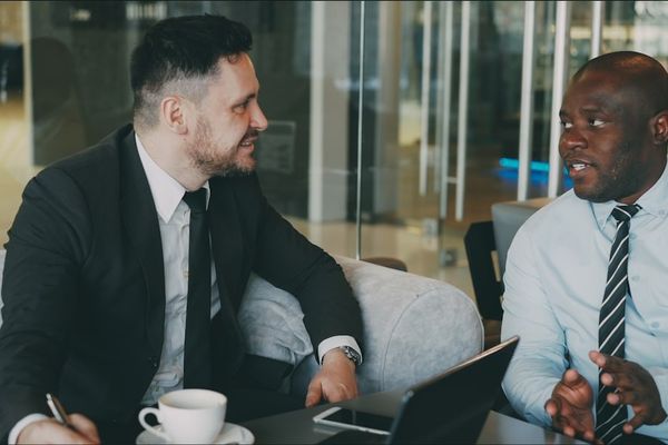 Two businessmen in suits talking at a table.