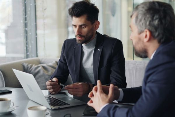 a couple of men sitting at a table with laptops
