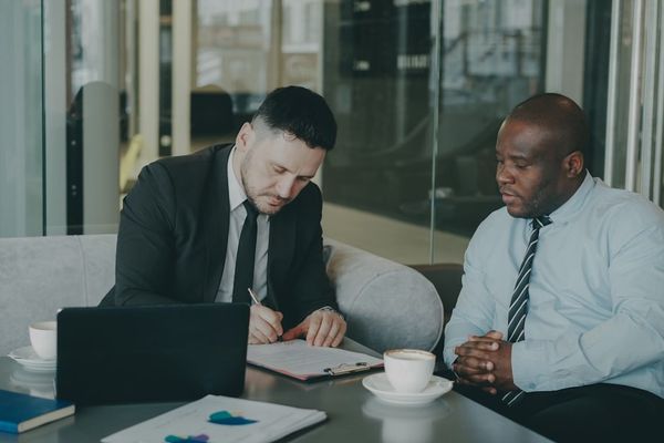 Two businessmen signing a document at a table.