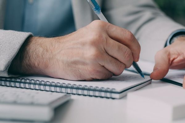A man in a suit writing on a notebook