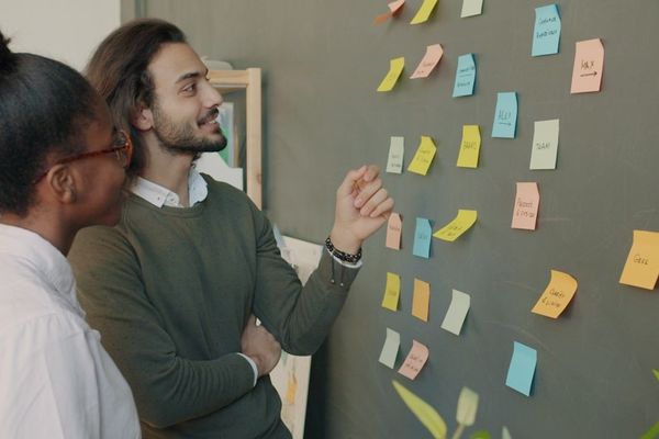 Two colleagues discuss sticky notes on a wall.