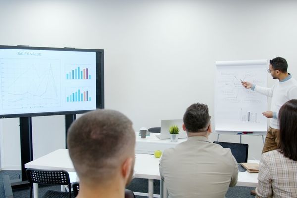 Man presents charts to seated audience in a modern office.