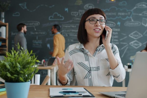 Woman talking on phone in modern office with chalkboard wall.