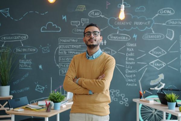 Man standing with arms crossed in front of chalkboard.