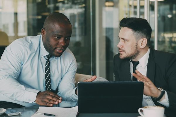 Two businessmen collaborating over a tablet and laptop.