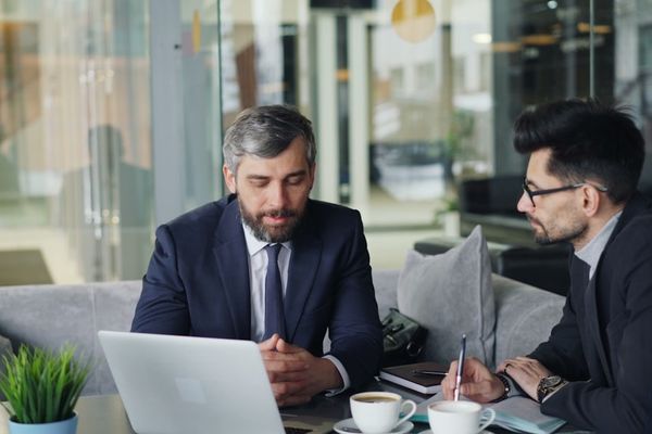 two men sitting at a table working on a laptop