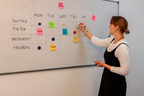 a woman writing on a white board with sticky notes