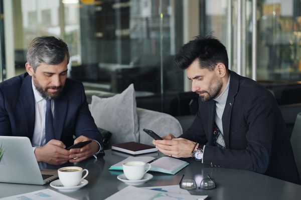 two men sitting at a table looking at their phones