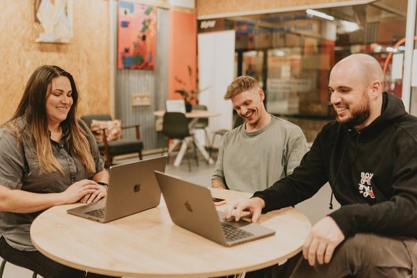 Three people collaborate around a table with laptops.