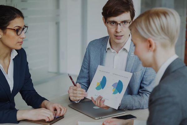 Three professionals discussing charts in a meeting.