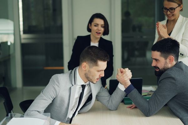 Two businessmen arm wrestling while colleagues watch