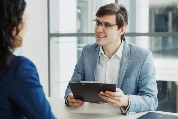 Man in suit interviews woman holding clipboard.