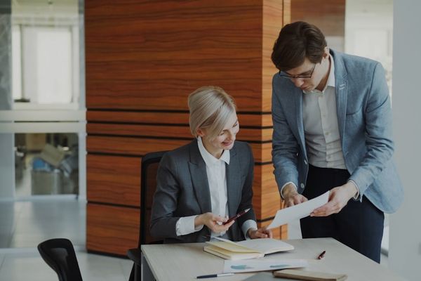 Two colleagues discussing documents at an office desk.