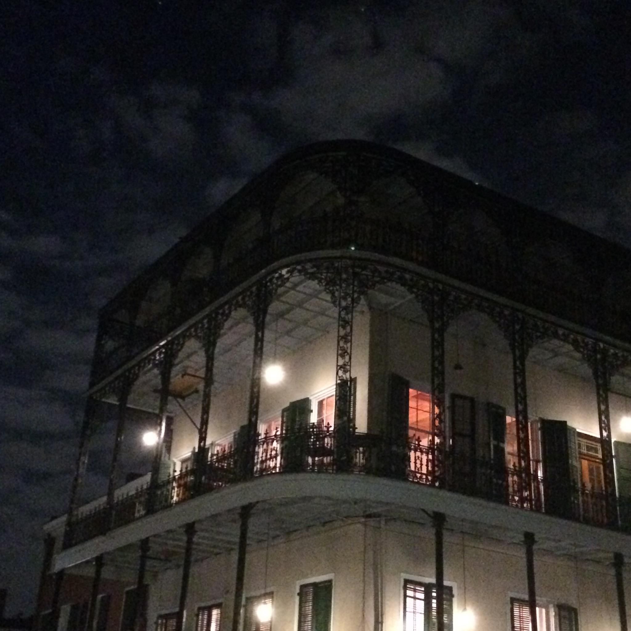 French Quarter building with ornate iron balcony lit warmly against night sky