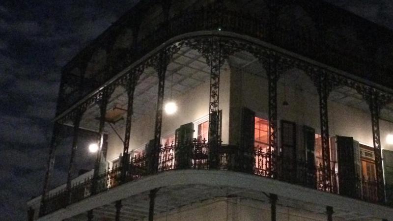 French Quarter building with ornate iron balcony lit warmly against night sky