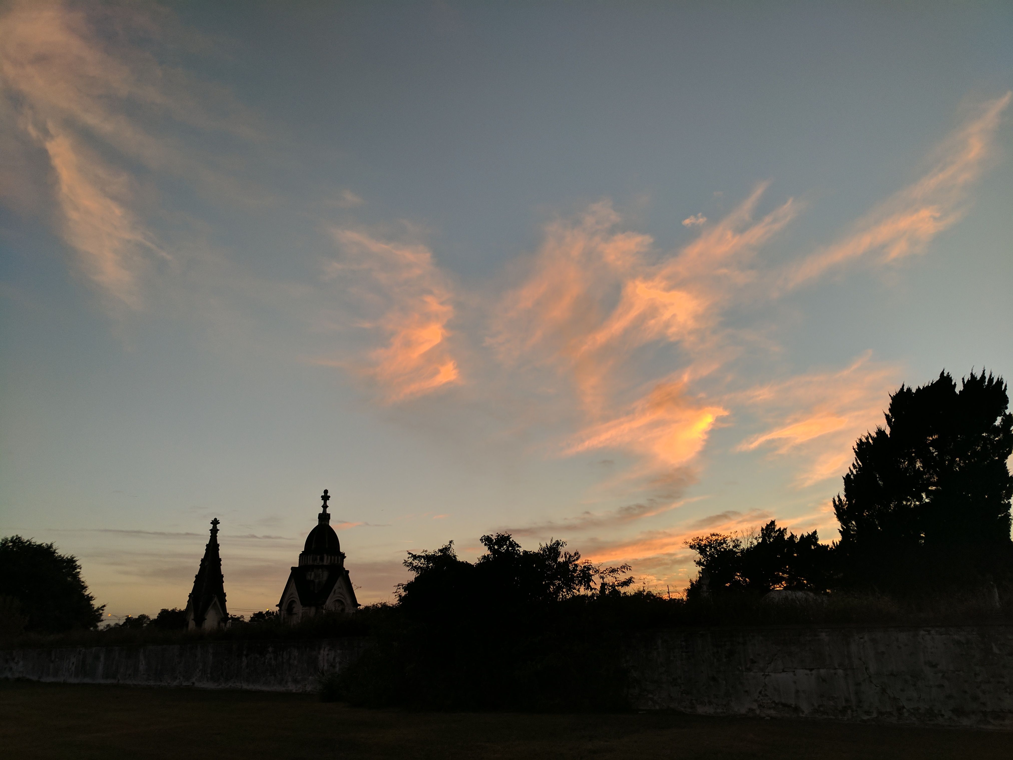 Cemetery mausoleum silhouettes against dramatic orange sunset sky