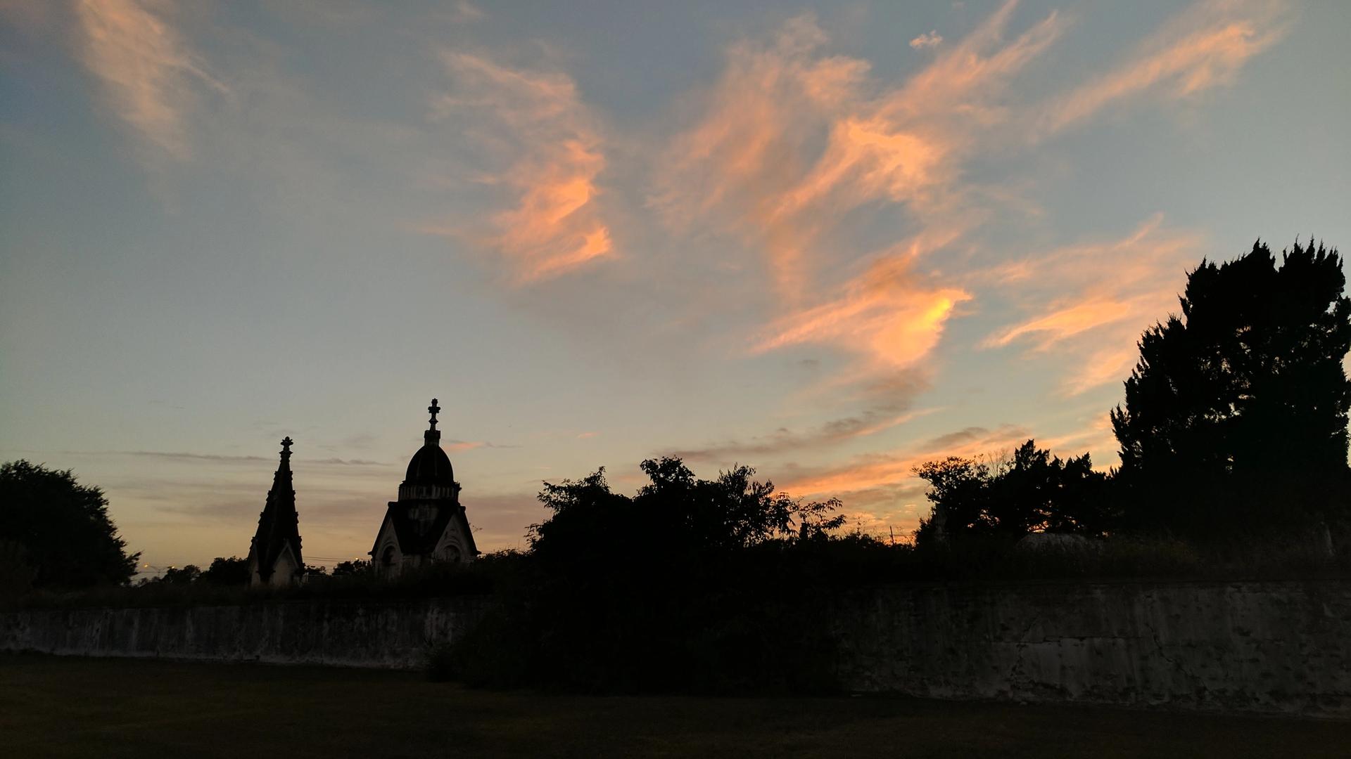 Cemetery mausoleum silhouettes against dramatic orange sunset sky