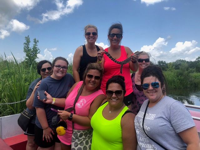 Group of women holding snake and smiling on large airboat swamp tour