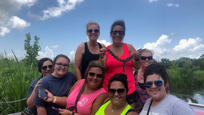 Group of women holding snake and smiling on large airboat swamp tour