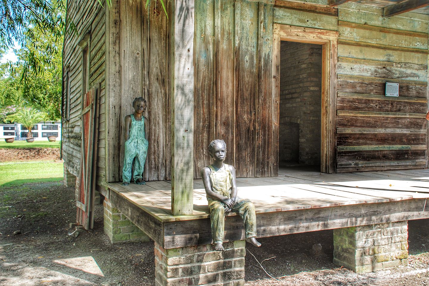 Bronze sculptures of two enslaved children on the porch of a Whitney Plantation cabin