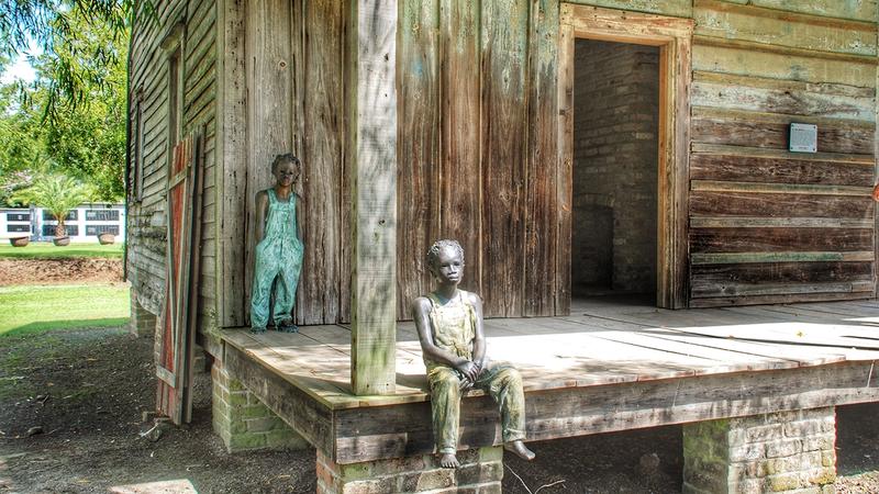 Bronze sculptures of two enslaved children on the porch of a Whitney Plantation cabin