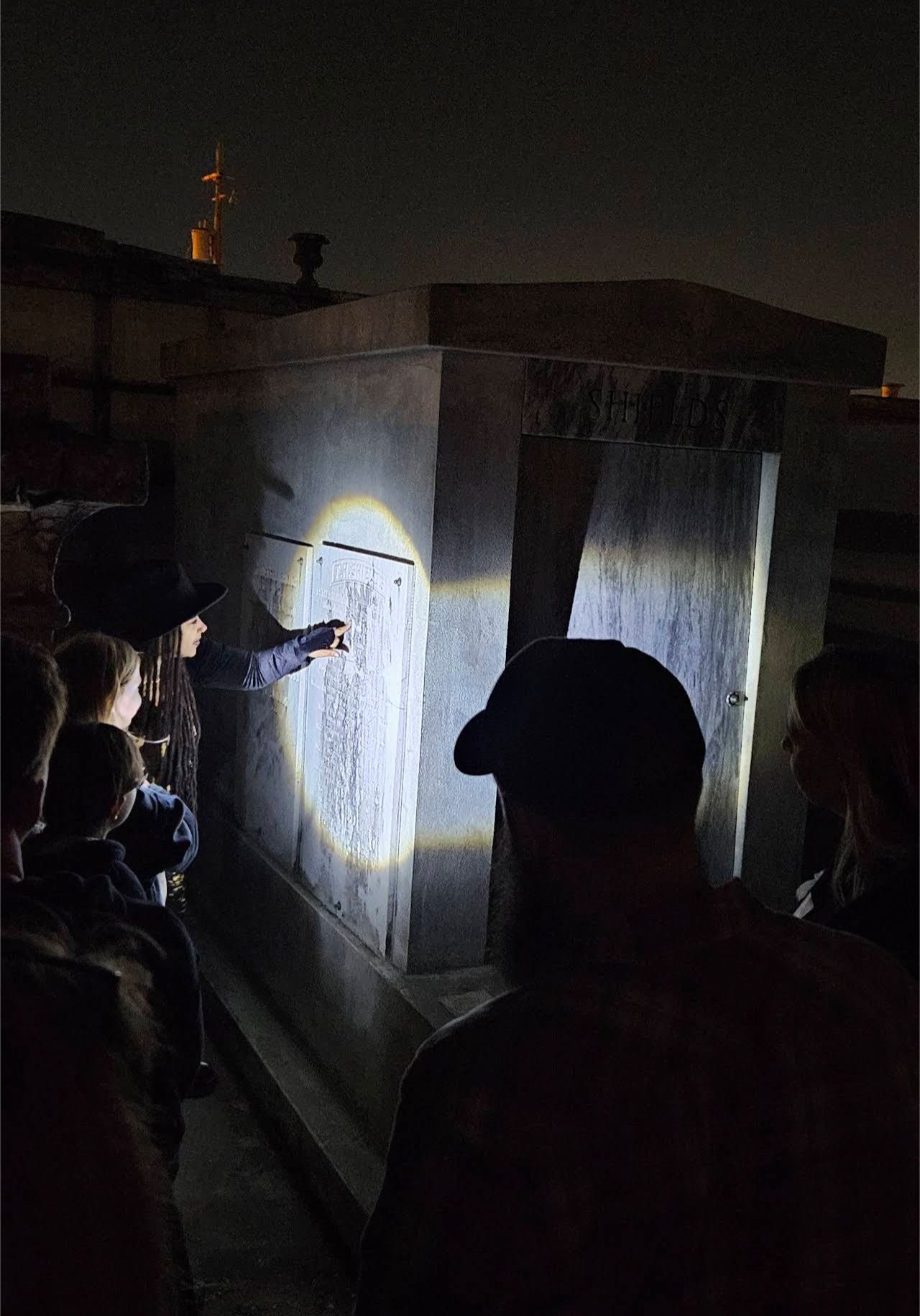 Tour guide shining flashlight on historic tomb while guests watch at night