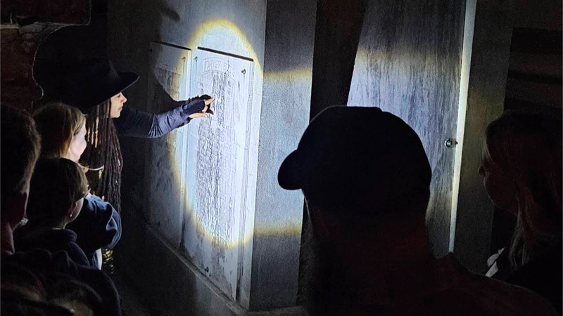Tour guide shining flashlight on historic tomb while guests watch at night