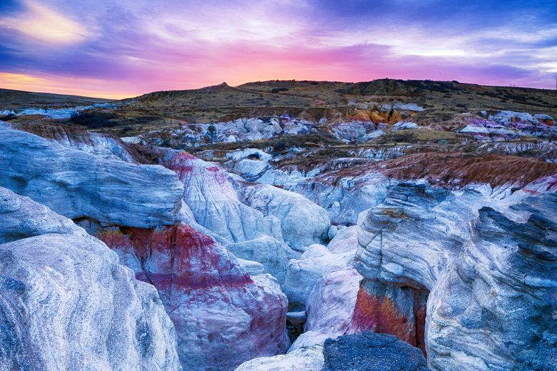 Layered white and pink rock formations under a purple sunset sky at Paint Mines Interpretive Park in Colorado.
