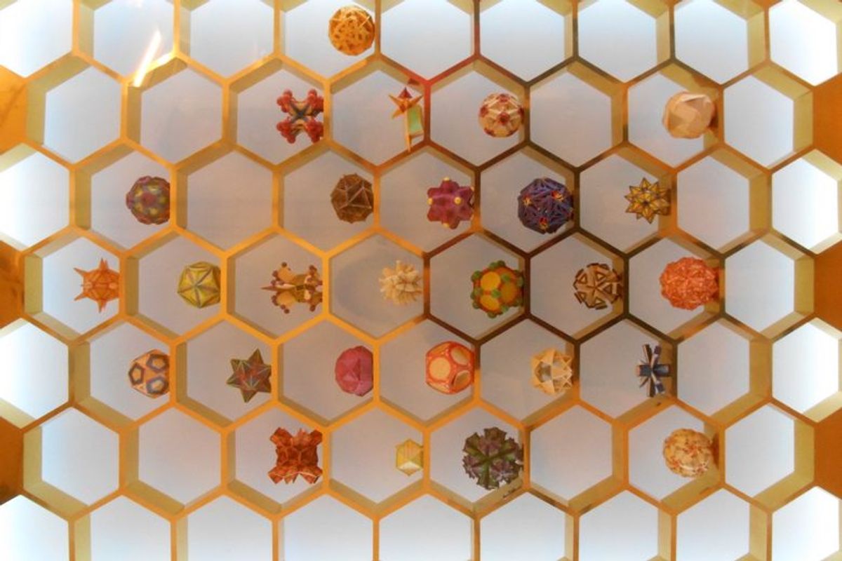 A wall display of colorful geometric shapes and polyhedra set within a large golden honeycomb-patterned grid.